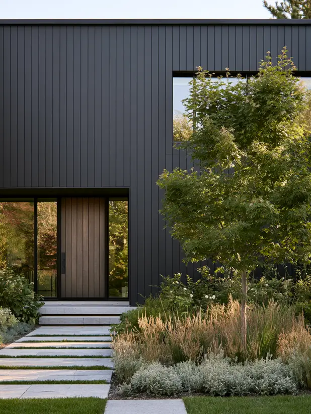 Modern black house exterior with matte vertical siding, warm wood-slatted front door and a naturalistic garden path