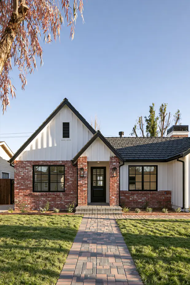 Single-story modern ranch with red brick lower walls, white board-and-batten gable, black windows, and a brick paver walkway