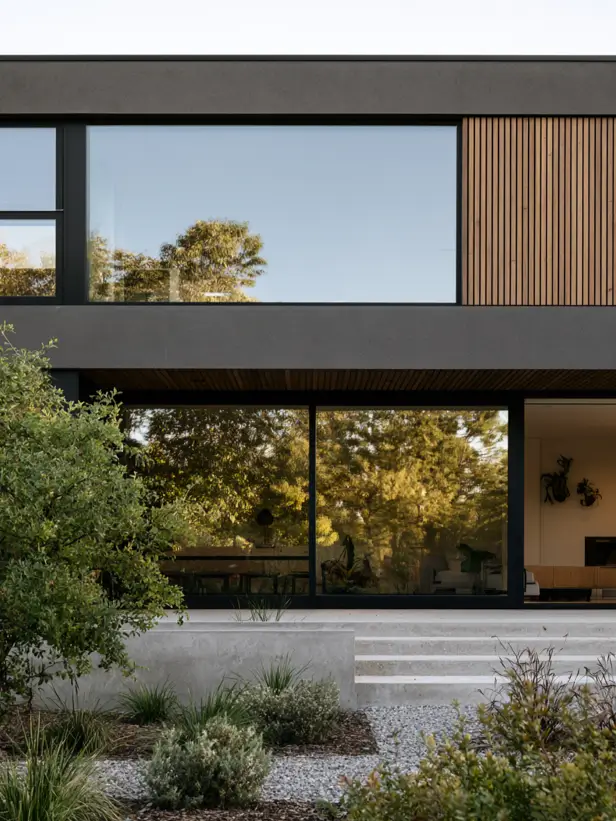 Modern charcoal house exterior with vertical timber batten cladding, black-framed floor-to-ceiling glass and drought-tolerant planting