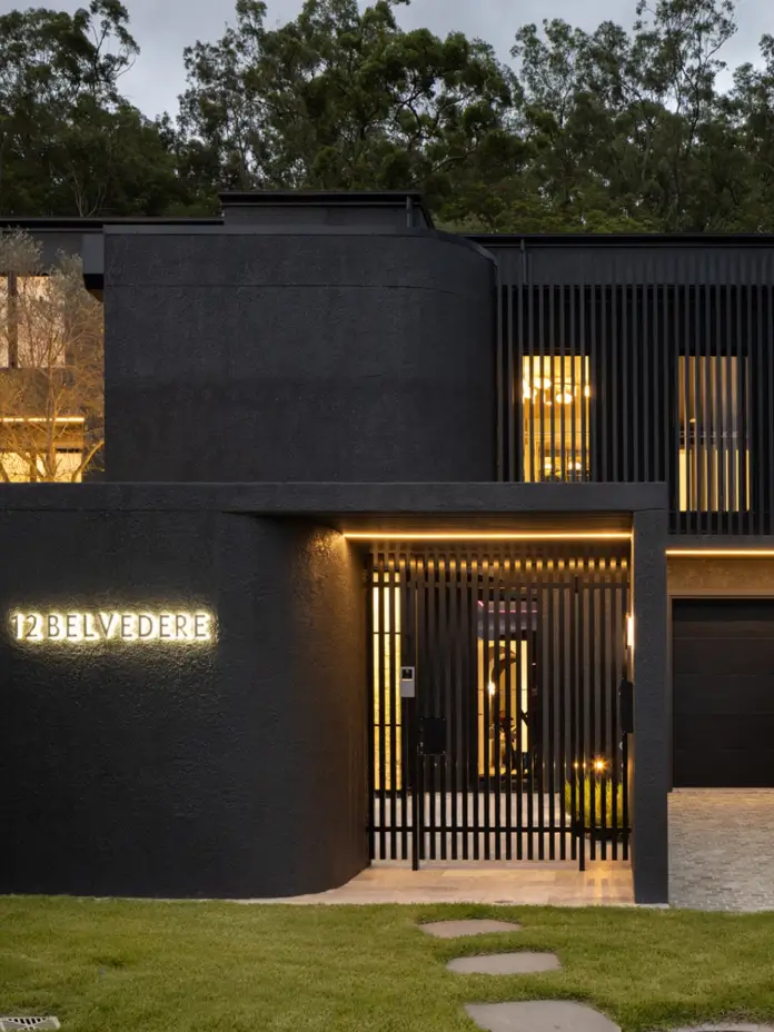 Black rendered house exterior at dusk with warm-lit timber batten screens and backlit house numbers