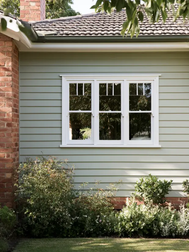Pale sage green weatherboard house exterior with red brick chimney and white window trim