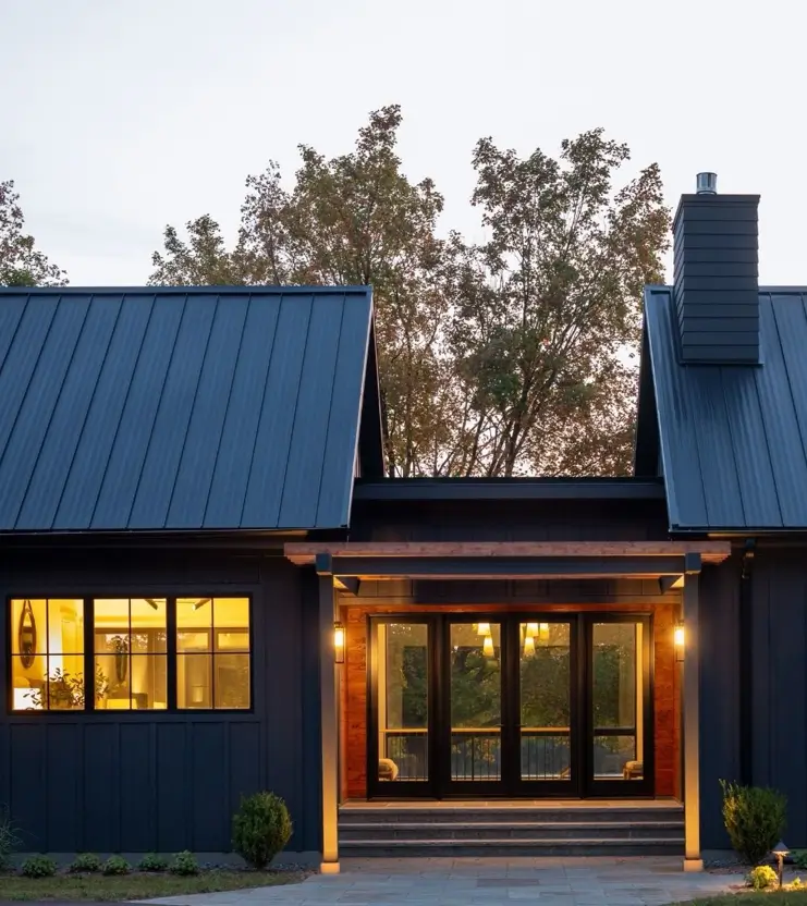 Near-black board-and-batten house exterior with a warm cedar-lined entry porch glowing at dusk