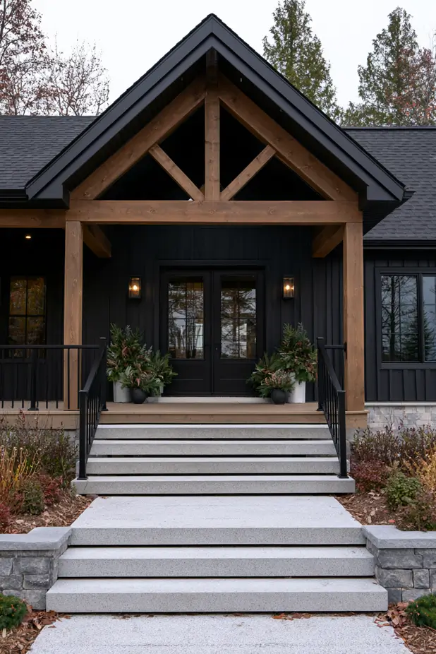 Black board-and-batten house exterior with a timber-truss gable porch, granite steps and stone planters