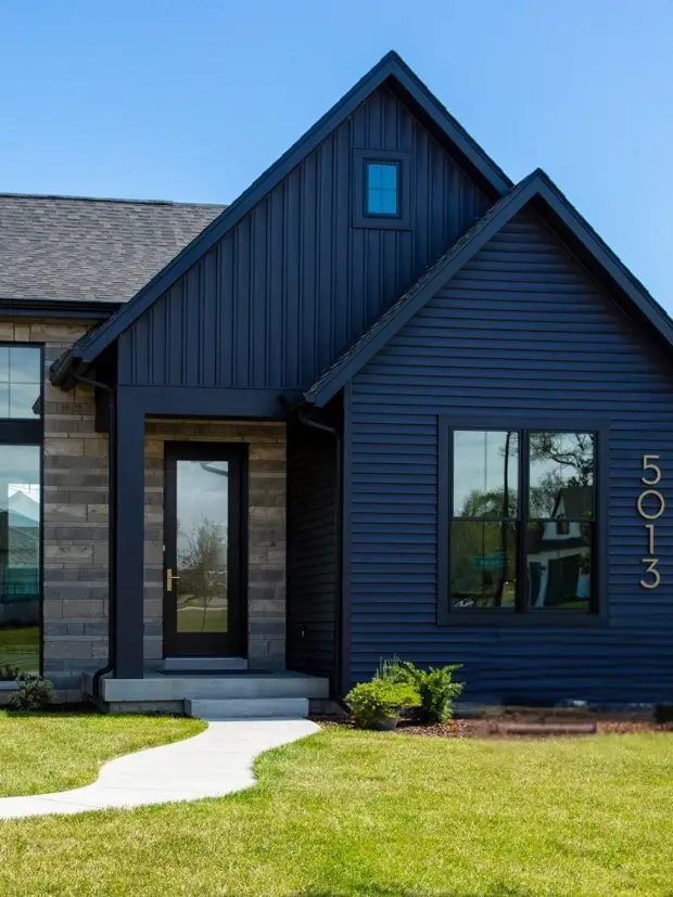 Navy-black modern farmhouse exterior with board-and-batten and lap siding, stone entry and gold house numbers