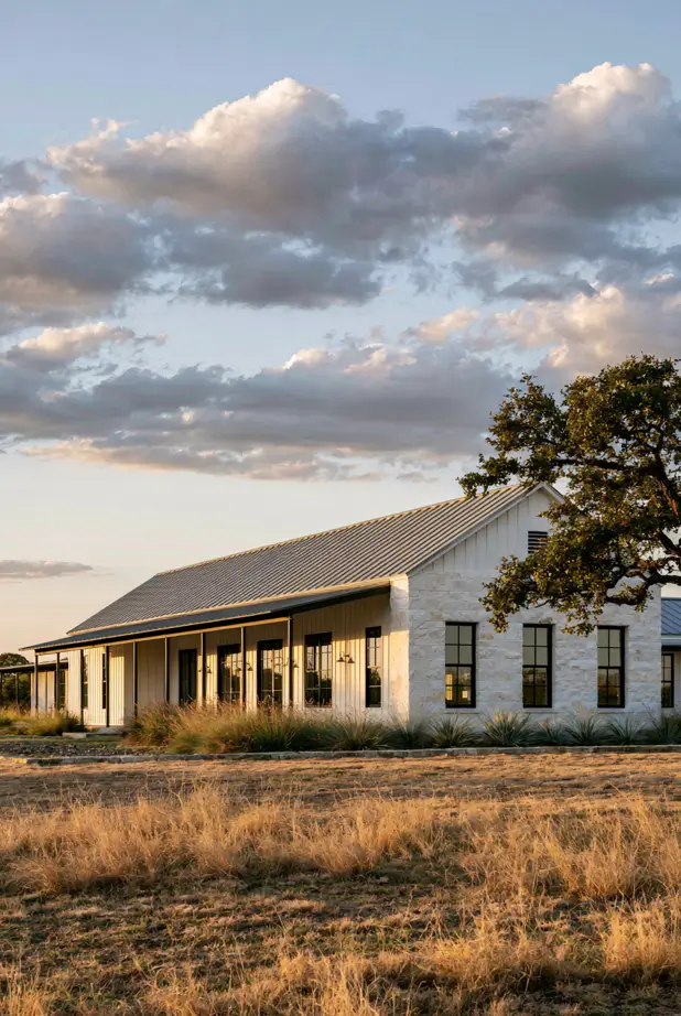 Long low single-story ranch with a full-length covered porch, standing-seam metal roof, stone and board-batten, at sunset