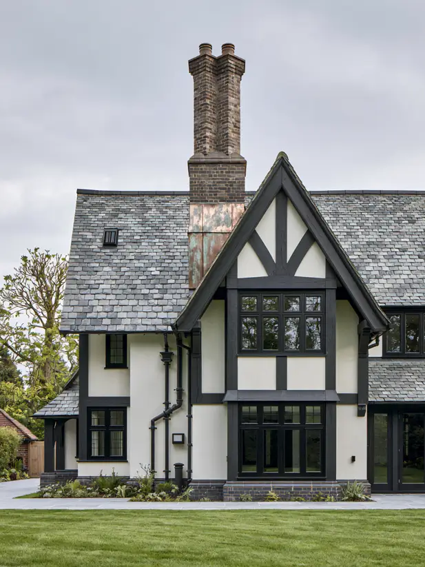 Modern Tudor with white stucco, a black standing seam metal roof and a dark timber gable