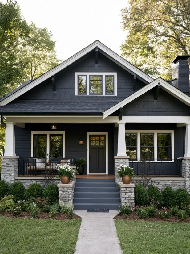Dark charcoal Craftsman bungalow exterior with white porch columns, stone piers and twin gables
