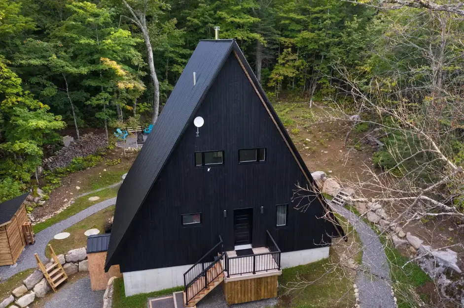 Black A-frame cabin exterior with charred timber cladding set in a forest, aerial view