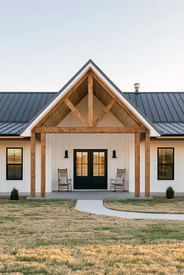 Single-story white ranch entry at dusk with a cedar timber-truss covered porch, rocking chairs, black doors, metal roof
