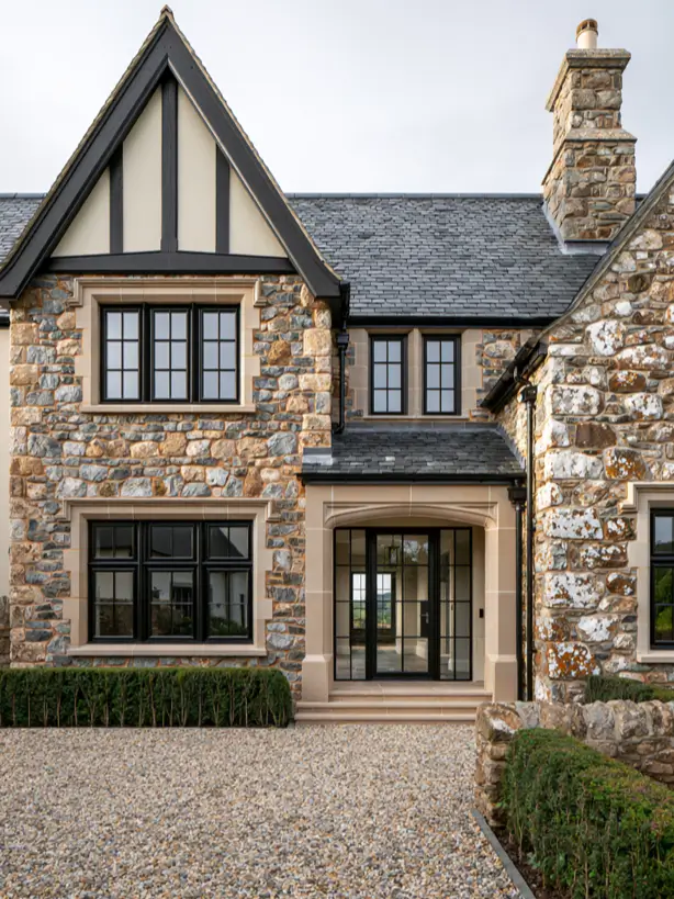 Stone modern Tudor with pale surrounds, black windows and a slate roof