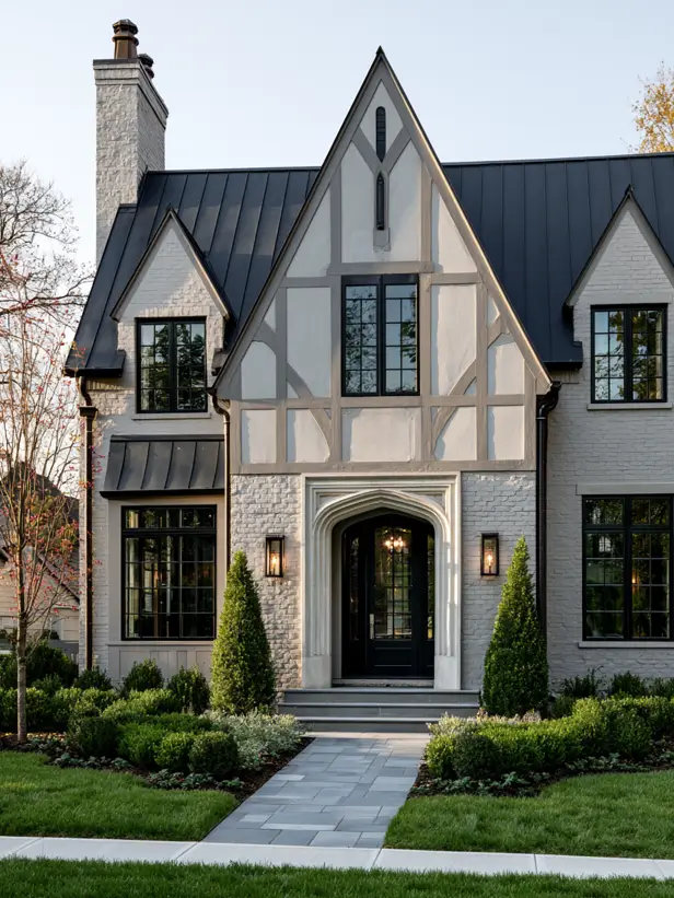 Pale limewashed brick modern Tudor with a black metal roof and an arched entry
