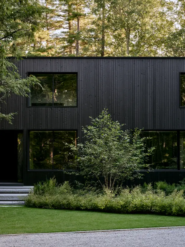 Black charred timber house exterior in a forest with large picture windows reflecting the trees