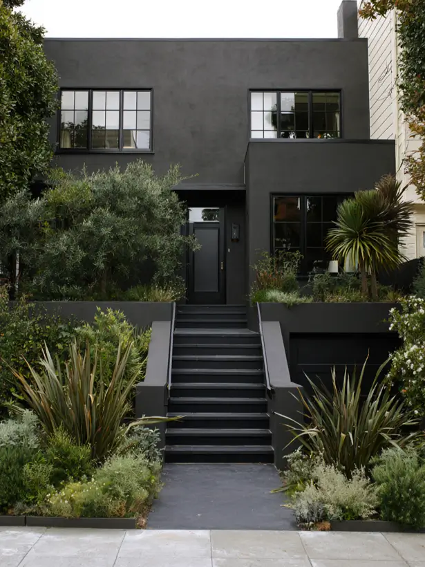 Charcoal stucco townhouse exterior with black steel windows and terraced Mediterranean planting