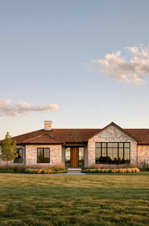 Long low single-story ranch in whitewashed brick with a clay-tile roof, black windows, and grasses lining the foundation