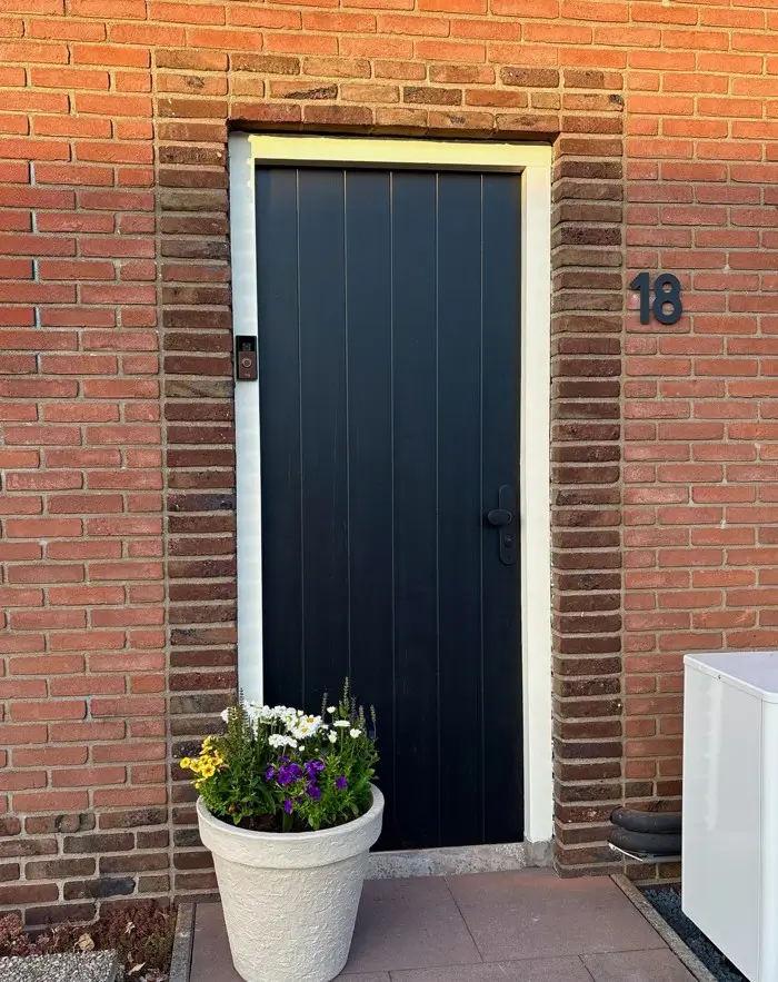 Near-black plank front door with pale surround against warm red brick, one of the best front door colors for red brick houses.