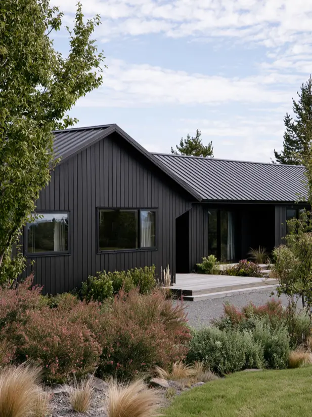 Black barn-style house exterior with vertical shiplap cladding, standing-seam metal roof and dusky pink planting