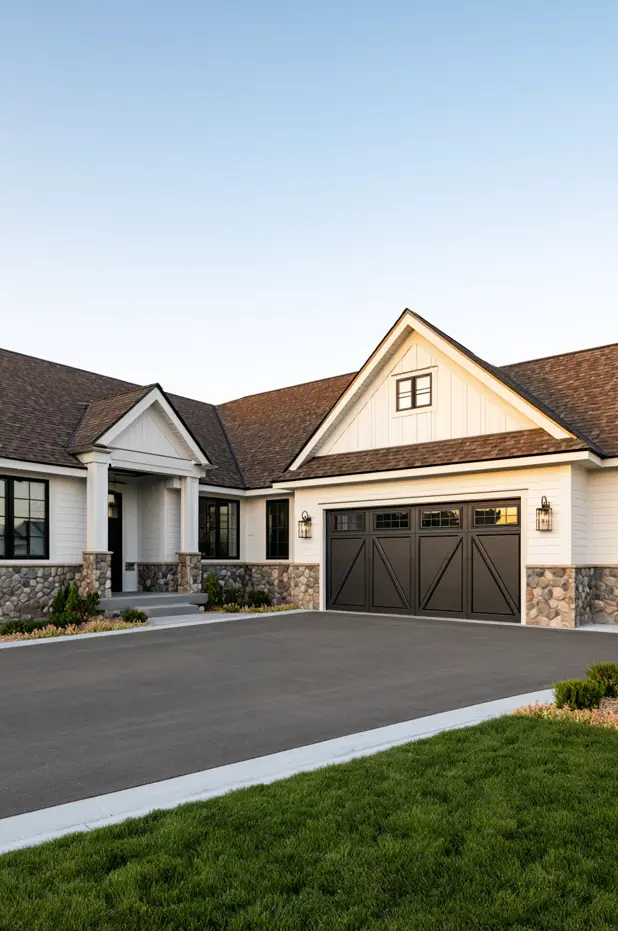 Single-story white ranch with a river-rock stone base, black windows, carriage garage door, and a gabled entry portico