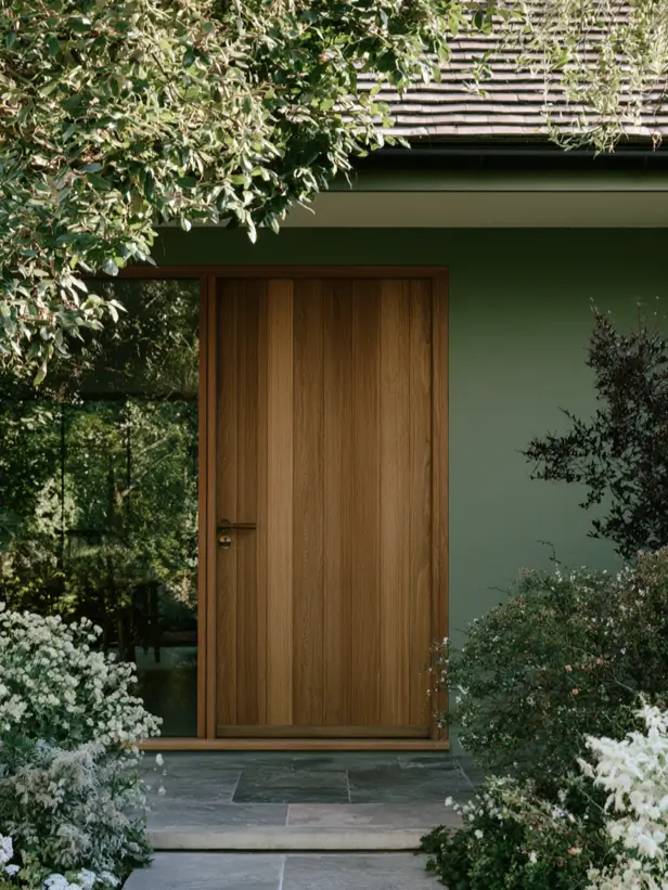 Natural oak wood front door against a deep sage green house exterior