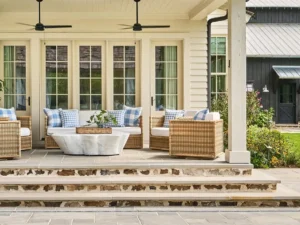 Covered front porch with woven rattan seating and blue-and-white checked pillows on a cream board-and-batten farmhouse — small front porch ideas.